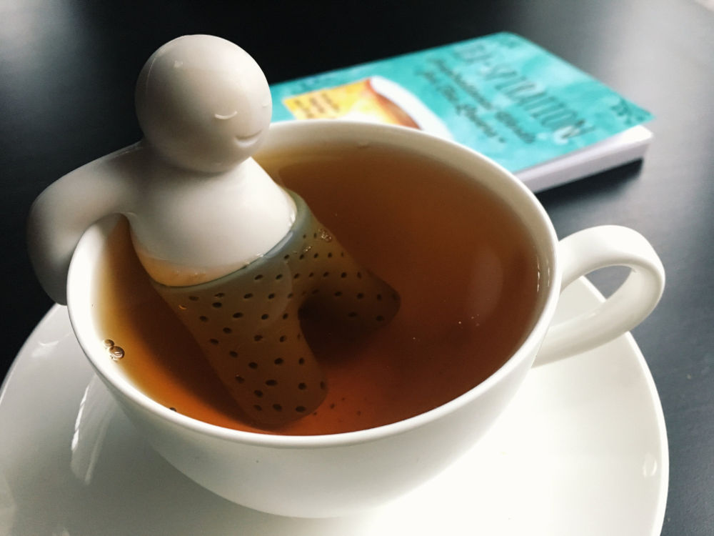 Una tazza di tè con l'omino infusore e un libro (Tea-spiration by Lu Ann Pannunzio)
